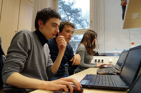 Drei Kamaros sitzen an einem langen Schreibtisch und haben jeweils einen Laptop vor sich